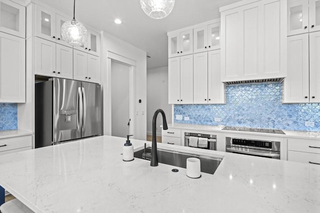 kitchen with stainless steel appliances, light stone counters, sink, white cabinetry, and decorative light fixtures