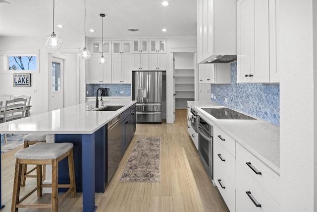 kitchen with hanging light fixtures, a kitchen island with sink, white cabinetry, appliances with stainless steel finishes, and sink