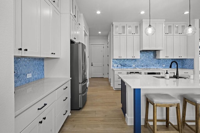 kitchen with sink, white cabinetry, stainless steel refrigerator, hanging light fixtures, and a breakfast bar