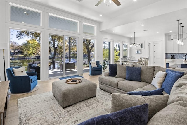 living room with light wood-type flooring, a water view, and ceiling fan with notable chandelier