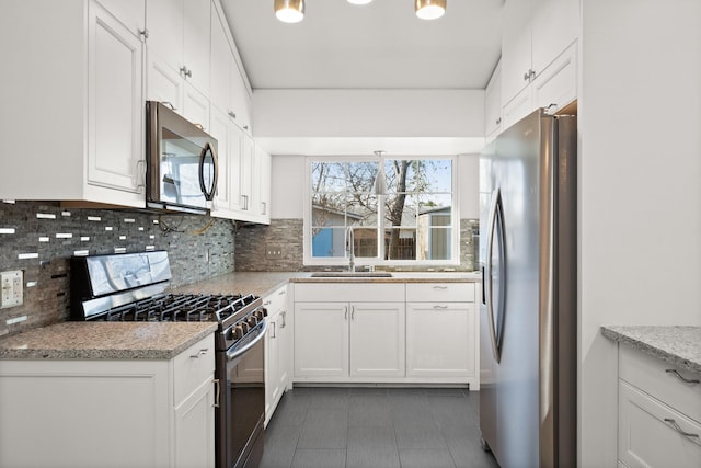 kitchen featuring appliances with stainless steel finishes, light stone countertops, decorative backsplash, white cabinets, and sink