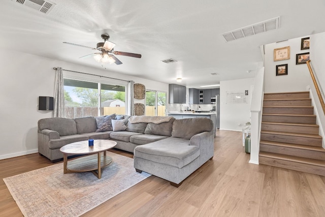 living room with a textured ceiling, ceiling fan, and light hardwood / wood-style flooring