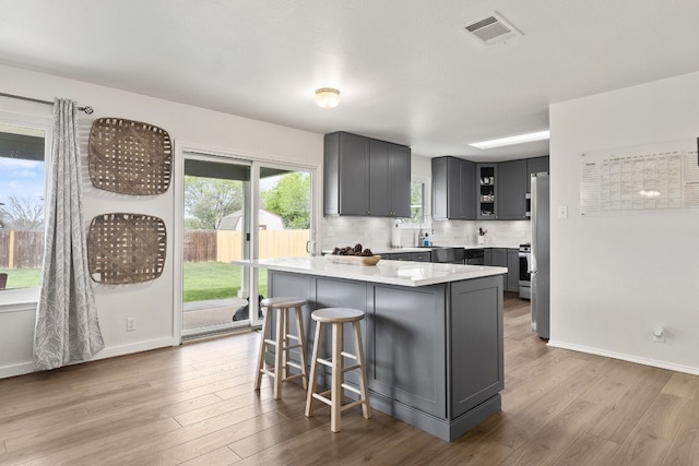 kitchen with stainless steel refrigerator, decorative backsplash, a breakfast bar area, and light hardwood / wood-style flooring