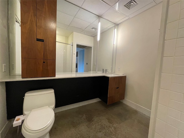 bathroom featuring concrete floors, toilet, vanity, and a drop ceiling