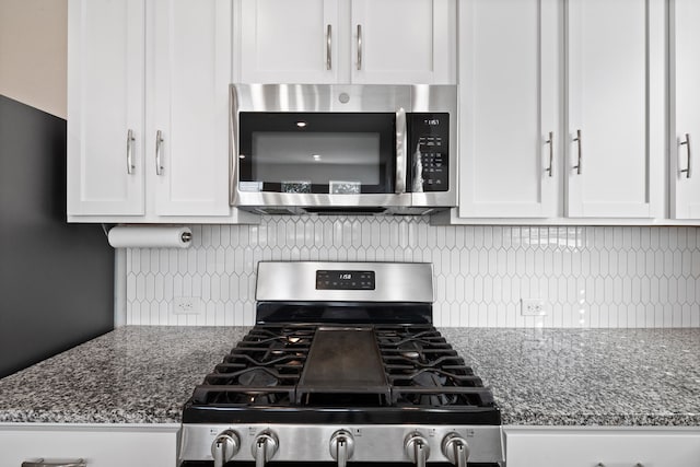 kitchen with stainless steel appliances, dark stone countertops, tasteful backsplash, and white cabinetry