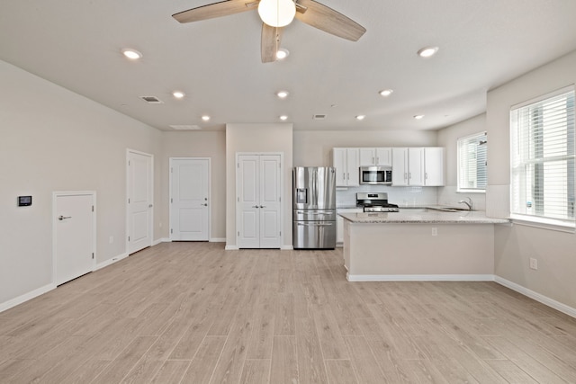 kitchen with appliances with stainless steel finishes, light stone countertops, kitchen peninsula, sink, and white cabinetry