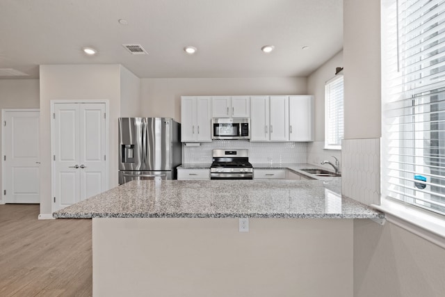 kitchen featuring stainless steel appliances, kitchen peninsula, light stone countertops, sink, and white cabinetry