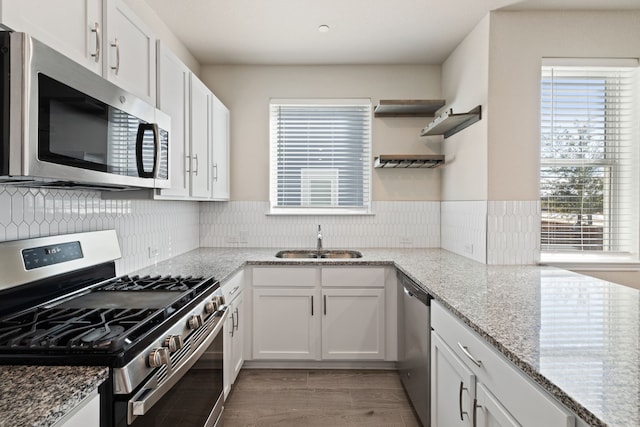 kitchen with stainless steel appliances, light stone countertops, white cabinetry, and sink