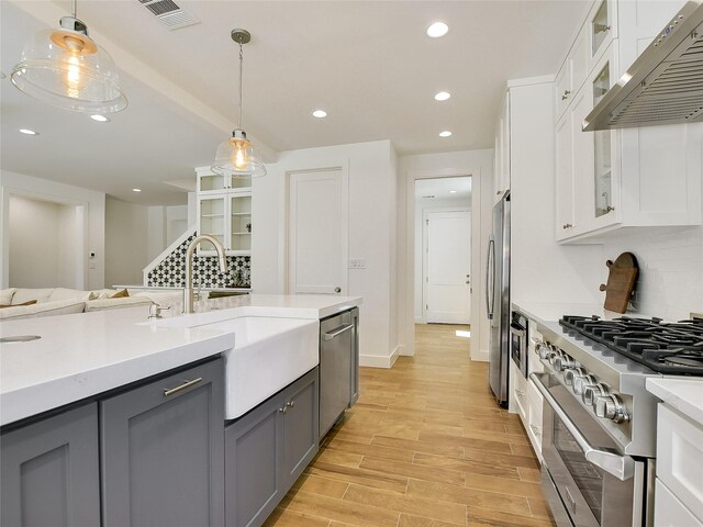 kitchen featuring decorative light fixtures, white cabinetry, exhaust hood, and appliances with stainless steel finishes