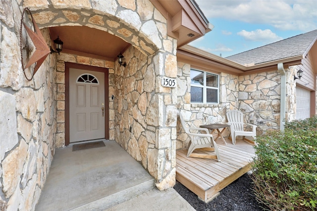 entrance to property with a garage, stone siding, and a shingled roof