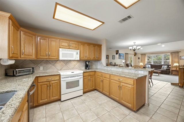 kitchen with light tile patterned floors, white appliances, light stone counters, kitchen peninsula, and an inviting chandelier