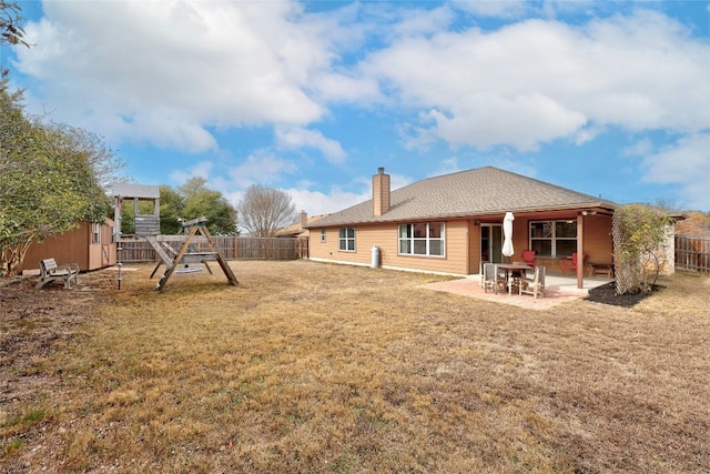 rear view of property featuring a playground, a patio, a chimney, a lawn, and a fenced backyard