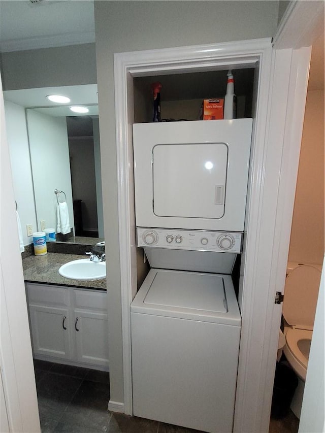 laundry room featuring sink, stacked washing maching and dryer, and dark tile patterned floors