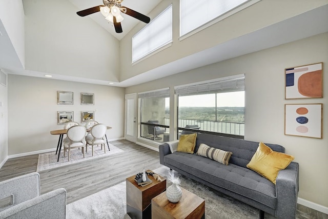 living room with ceiling fan, a towering ceiling, and hardwood / wood-style flooring