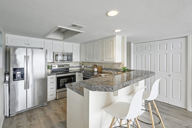 kitchen featuring stainless steel appliances, kitchen peninsula, a kitchen bar, sink, and white cabinetry