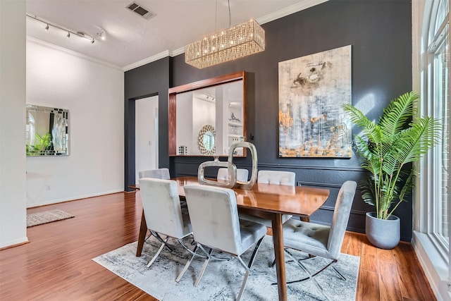 dining area featuring a notable chandelier, track lighting, ornamental molding, and hardwood / wood-style floors