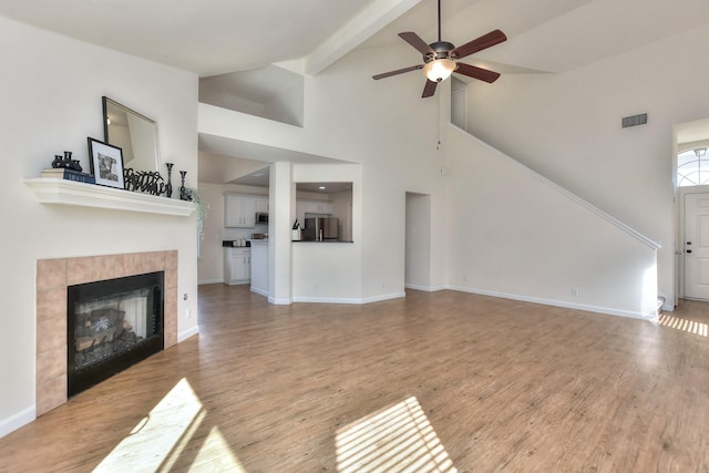 unfurnished living room featuring hardwood / wood-style floors, a tiled fireplace, ceiling fan, high vaulted ceiling, and beam ceiling