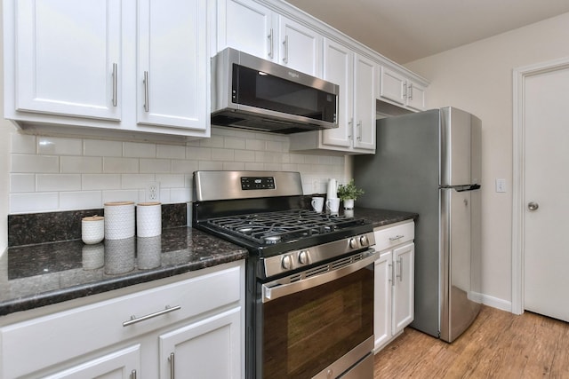 kitchen featuring stainless steel appliances, white cabinetry, light hardwood / wood-style floors, backsplash, and dark stone counters