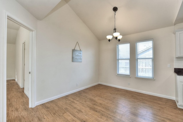 unfurnished dining area with a notable chandelier, light wood-type flooring, and vaulted ceiling