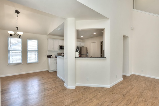 kitchen featuring a notable chandelier, stainless steel appliances, white cabinetry, and light wood-type flooring