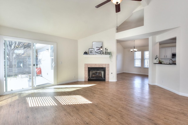 unfurnished living room with wood-type flooring, a fireplace, sink, lofted ceiling, and ceiling fan with notable chandelier