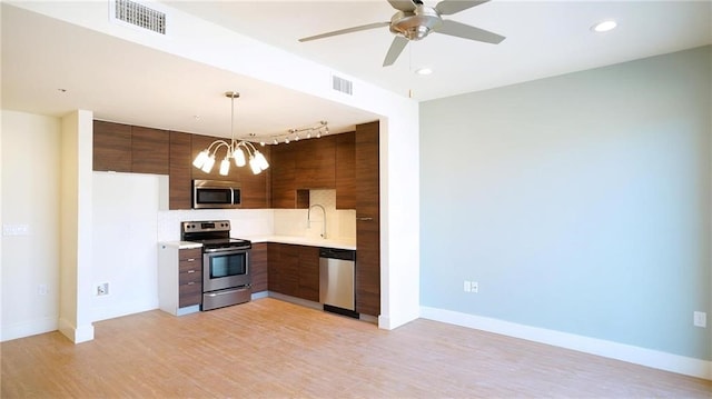 kitchen with ceiling fan with notable chandelier, appliances with stainless steel finishes, backsplash, hanging light fixtures, and light hardwood / wood-style flooring