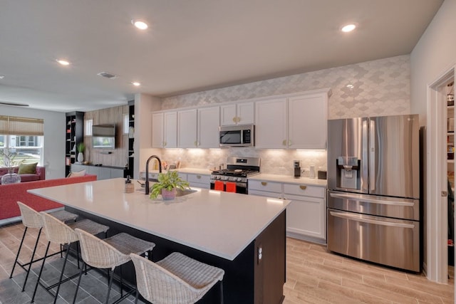 kitchen with stainless steel appliances, a kitchen island with sink, and white cabinetry