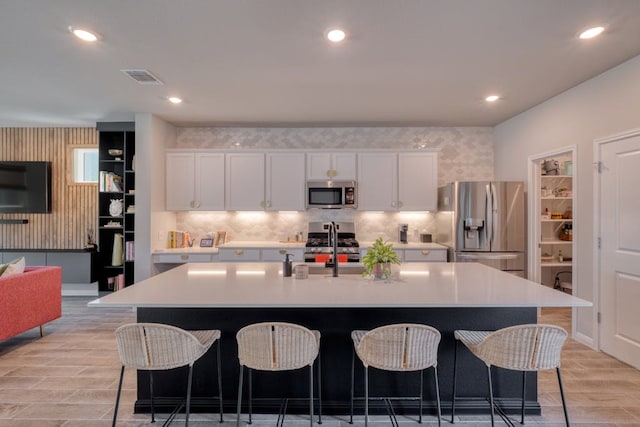 kitchen with light hardwood / wood-style flooring, stainless steel appliances, a kitchen bar, a kitchen island with sink, and white cabinetry