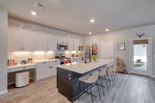 kitchen featuring stainless steel appliances, white cabinetry, and a kitchen island with sink