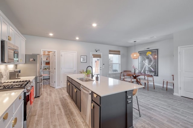 kitchen with decorative light fixtures, stainless steel appliances, an island with sink, white cabinetry, and sink