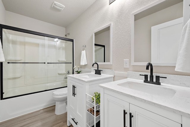 2213 Rocoso Trl, Leander, TX 78641 - full bathroom featuring toilet, two vanities, wood finished floors, a textured wall, and shower / bath combination with glass door