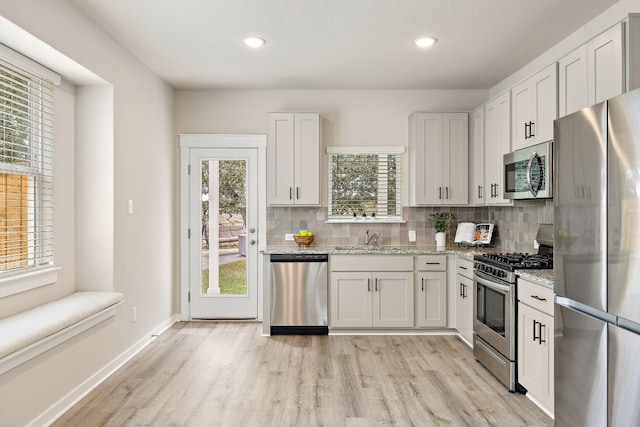 2213 Rocoso Trl, Leander, TX 78641 - kitchen featuring appliances with stainless steel finishes, backsplash, light wood finished floors, a sink, and light stone counters