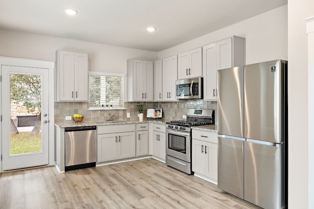 kitchen with backsplash, white cabinets, light stone countertops, and stainless steel appliances