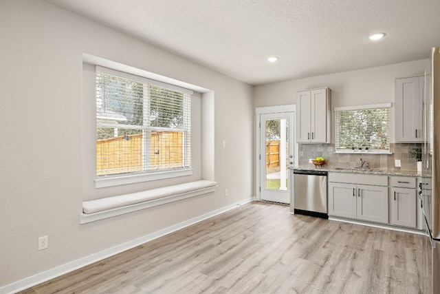 kitchen with light stone countertops, light hardwood / wood-style floors, tasteful backsplash, dishwasher, and a textured ceiling