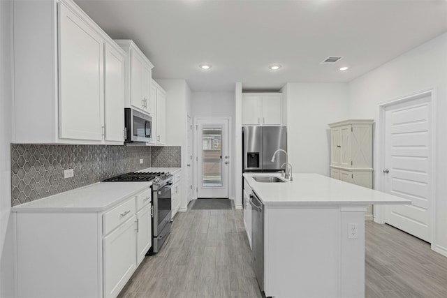 kitchen with visible vents, a center island with sink, stainless steel appliances, light wood finished floors, and a sink