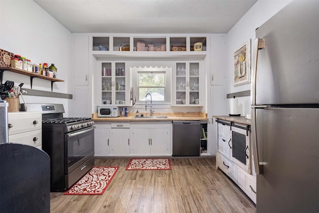 kitchen featuring a textured ceiling, white cabinetry, stainless steel appliances, sink, and light wood-type flooring