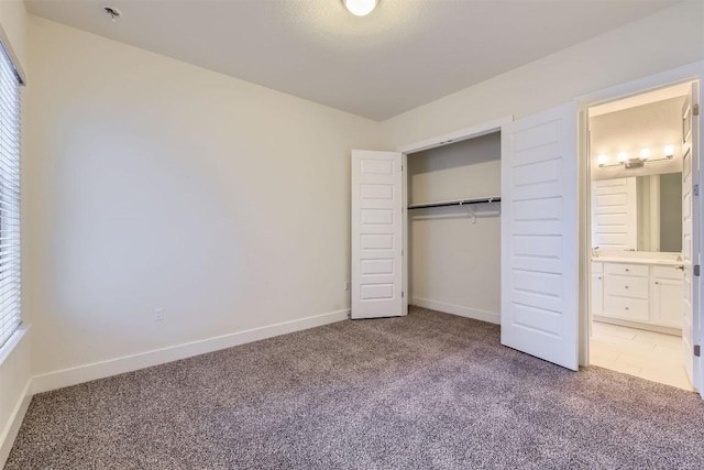 unfurnished bedroom featuring carpet floors, ensuite bath, baseboards, and a closet