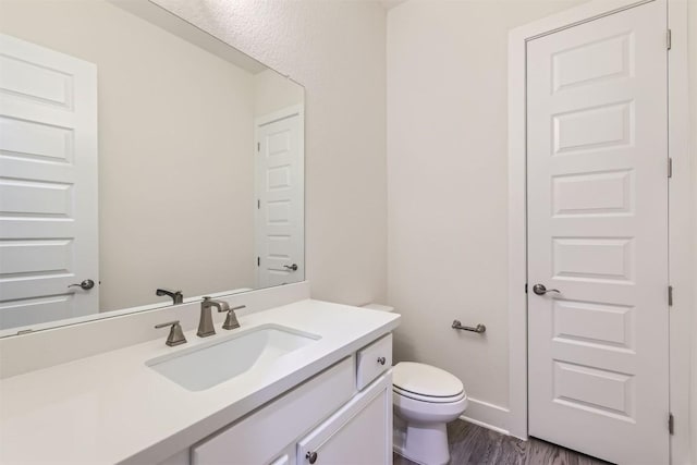 half bath featuring toilet, wood finished floors, vanity, and baseboards