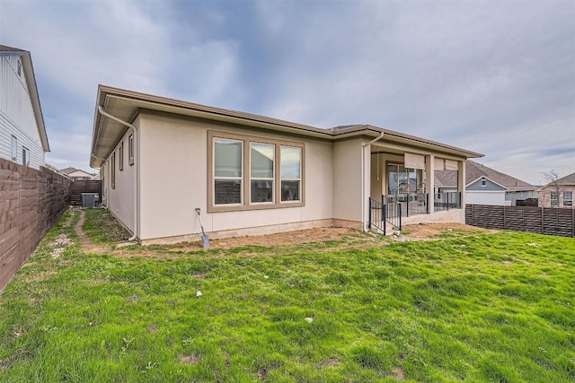 rear view of property featuring central air condition unit, stucco siding, a fenced backyard, and a yard