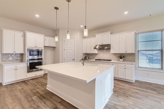 kitchen featuring light hardwood / wood-style flooring, hanging light fixtures, a center island with sink, white cabinets, and appliances with stainless steel finishes