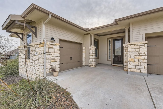 doorway to property featuring a garage, stone siding, and concrete driveway