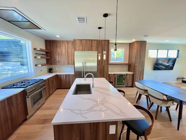 kitchen featuring premium appliances, decorative light fixtures, a center island with sink, wine cooler, and sink