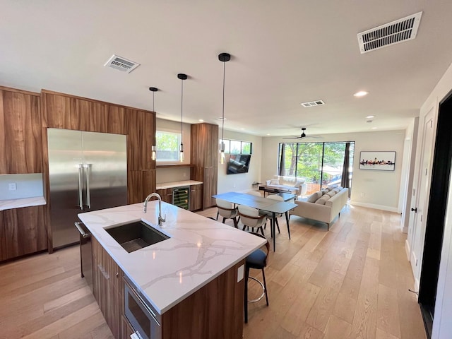 kitchen featuring hanging light fixtures, a kitchen island with sink, built in fridge, ceiling fan, and sink