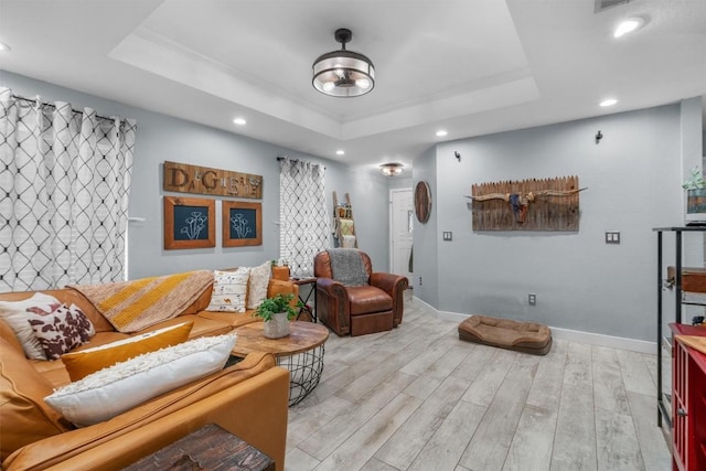 living room with a raised ceiling, crown molding, and light wood-type flooring