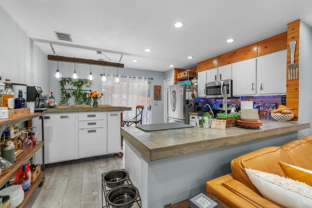 kitchen featuring pendant lighting, white cabinets, a kitchen breakfast bar, kitchen peninsula, and stainless steel appliances