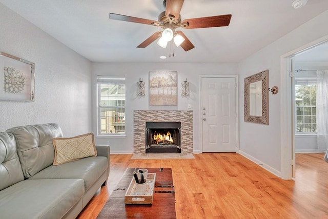 living area featuring a fireplace with flush hearth, baseboards, a ceiling fan, and wood finished floors