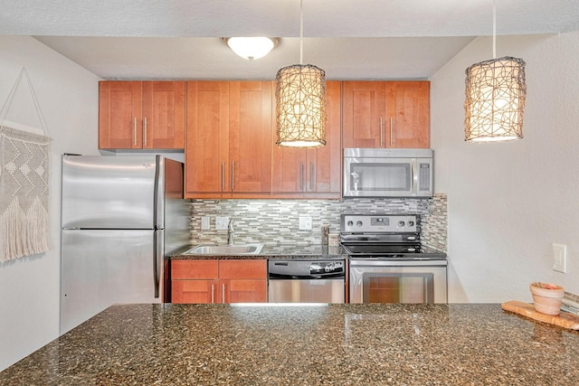 kitchen with stainless steel appliances, sink, dark stone countertops, decorative backsplash, and hanging light fixtures