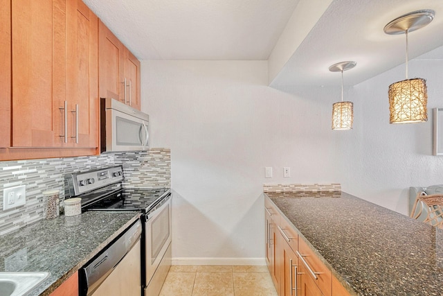 kitchen with decorative light fixtures, light tile patterned floors, backsplash, dark stone counters, and appliances with stainless steel finishes