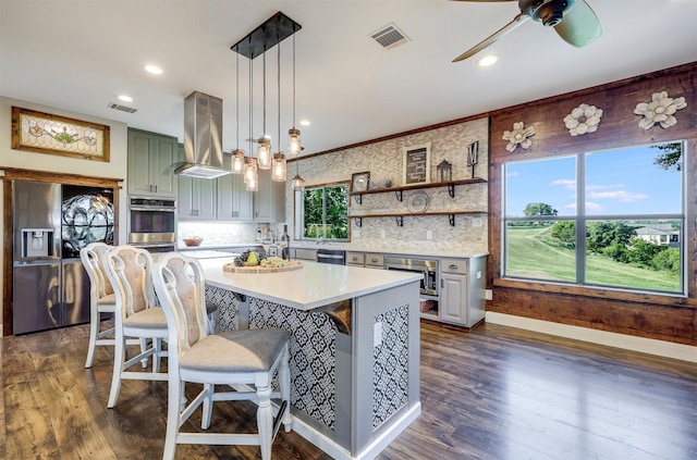 kitchen with island range hood, a center island, hanging light fixtures, backsplash, and appliances with stainless steel finishes