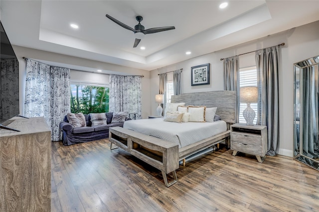 bedroom featuring wood-type flooring, multiple windows, ceiling fan, and a tray ceiling